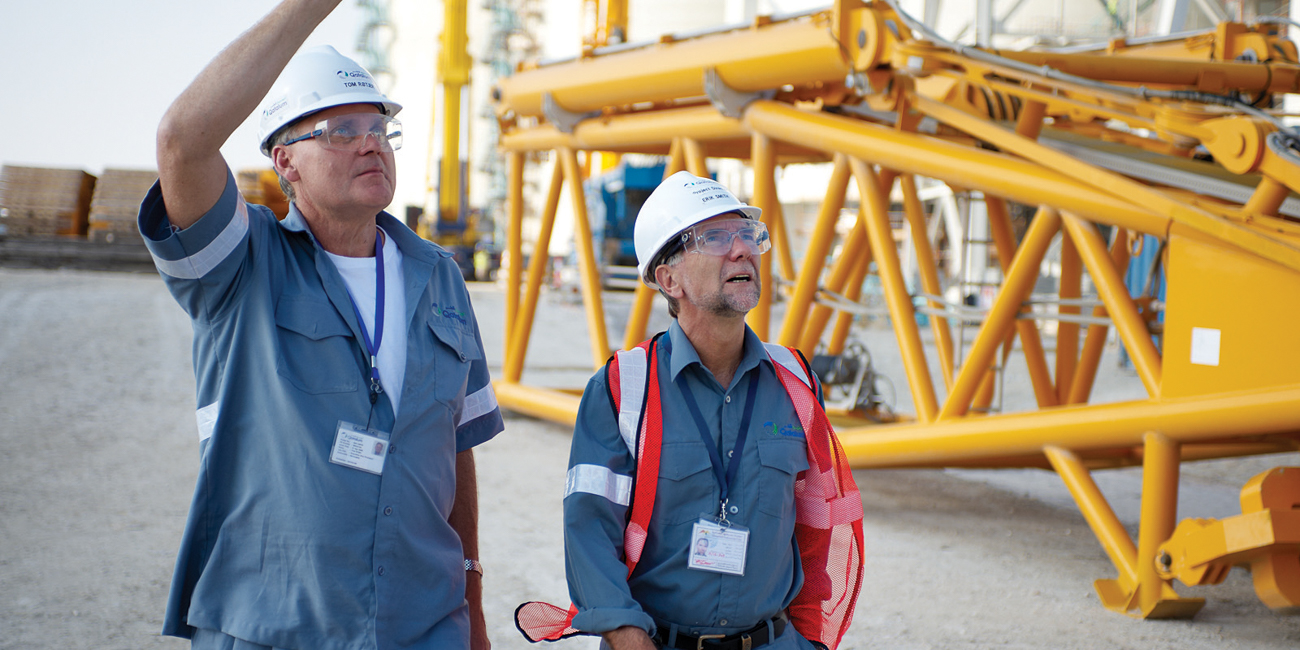 men wearing hard hats and standing in front of a yellow machine